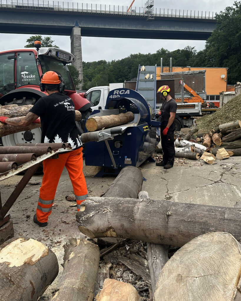 Mitarbeiter bedienen den Sägespaltautomaten, im Hintergrund werden Holzscheite ausgeworfen.